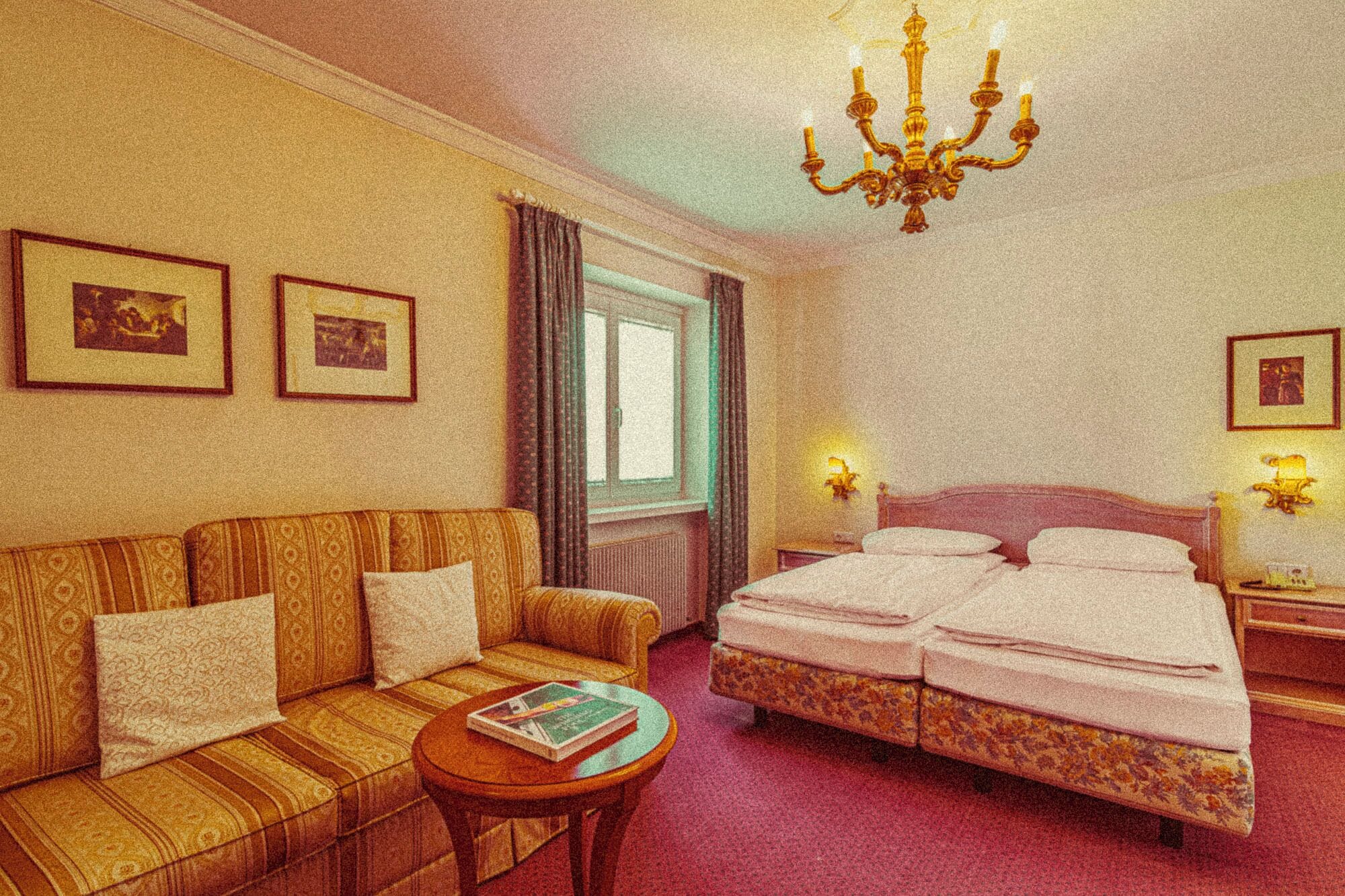 Habitación de hotel con sofá, cama, una mesita, candelabro y cuadros en las paredes.