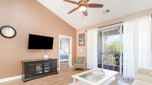 A living room with a television, a cabinet, a chair, a coffee table, and a sliding glass door to the outside.