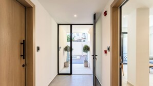 A modern hallway with a wooden door, a glass door leading to an outdoor area with potted plants, and a fire alarm on the wall. - Grec Suites Dafni, Athens by GrecCollection President Suite (Dafni)