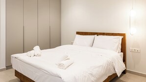 A neatly made bed with white linens and rolled towels, a wooden headboard, and a large wardrobe with sliding doors. - Grec Suites Dafni, Athens by GrecCollection President Suite (Dafni)