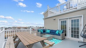 En tagterrasse med et træbord, en fletsofa med blå puder og udsigt over bybilledet.
