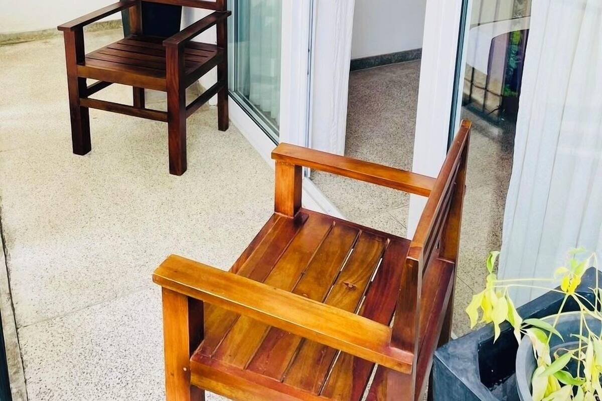 A wooden chair and table on a balcony with a potted plant and a sliding glass door.