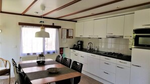 A modern kitchen with white cabinets, a black countertop, and a dining area with a wooden table and black chairs. - Lovely vacation home on beautiful park (Diever)