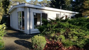 A modern, single-story building with a white exterior, large windows, and a covered outdoor area. - Lovely vacation home on beautiful park (Diever)