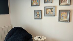 Una habitació amb una cadira negra, una taula petita blanca i sis quadres amb marc a la paret.