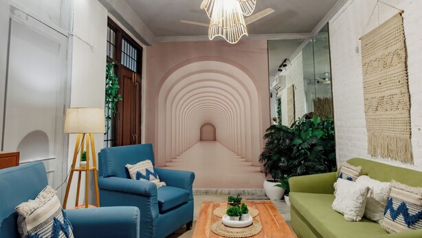 A living room with a blue armchair, a green sofa, a wooden coffee table, and a decorative wall with concentric circles. - 2BHK Tropical Haven Lajpat Nagar (New Delhi)