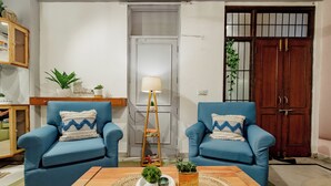 A living room with two blue armchairs, a wooden coffee table with decorative items, a floor lamp, and a wooden cabinet with plants. - 2BHK Tropical Haven Lajpat Nagar (New Delhi)