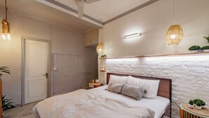 A bedroom with a large bed, a wooden headboard, a white wall with a textured design, a small bedside table with a lamp, and a ceiling fan. - 2BHK Tropical Haven Lajpat Nagar (New Delhi)