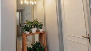 A hallway with a wooden console table holding potted plants, a hanging light fixture, and a white door. - 2BHK Tropical Haven Lajpat Nagar (New Delhi)