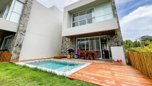 A modern house with a stone exterior, a swimming pool, and a patio area with outdoor furniture. - House with private pool in Beira Mar Condominium and private access to the beach. (São Miguel dos Milagres)