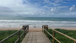 A wooden boardwalk leading to a beach with waves, under a partly cloudy sky. - House with private pool in Beira Mar Condominium and private access to the beach. (São Miguel dos Milagres)