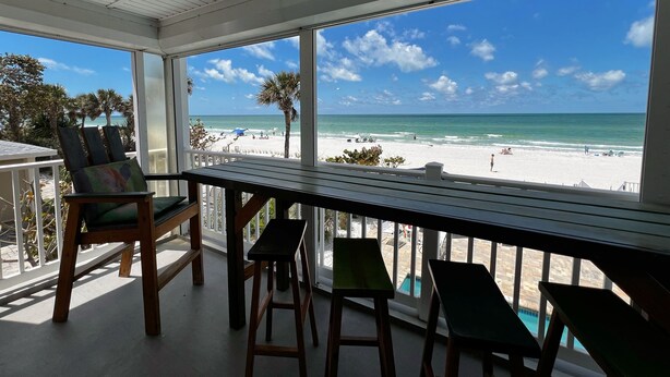 A covered outdoor area with a view of the beach, wooden furniture, and a pool.
