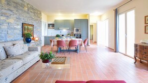 A cozy living room with a stone wall, a sofa, a coffee table with a chessboard, and a dining area with a table and chairs. - 2 bedroom amazing home in Sassetta (Sassetta)