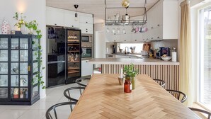 A modern kitchen with a central island, a dining area with a wooden table, and a black cabinet with glass doors.