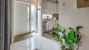 A modern kitchen with white cabinets, a dishwasher, and a sink. There is a plant on the right side and a door leading to another room.