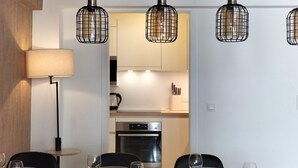 Un espace repas moderne avec une table dressée pour quatre personnes, une lampe et une cuisine en arrière-plan.