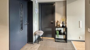 Un pasillo con una puerta oscura, un taburete pequeño y una repisa con objetos decorativos.