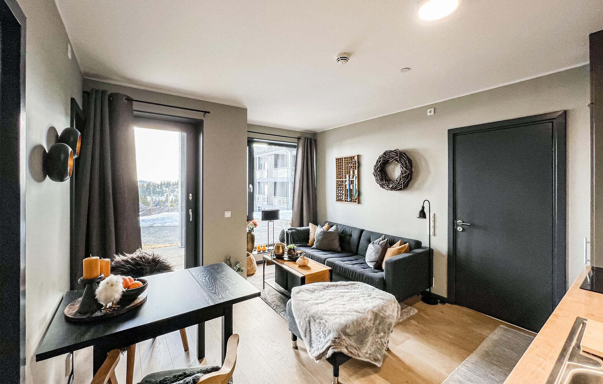 A modern living room with a sofa, a dining table, and a black door.
