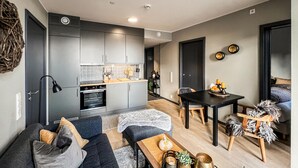 Una cocina moderna con armarios grises, horno empotrado y encimera de madera. Cuenta con un comedor con mesa y sillas, y una sala de estar con sofá y mesita de centro.