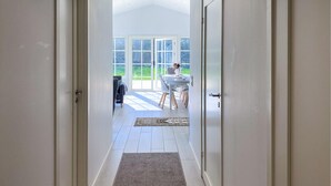 Een gang die uitkomt in een eetruimte met uitzicht op een tuin door grote ramen.