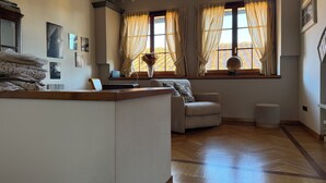 Una habitación con suelo de madera, un sofá, una silla, un escritorio con una computadora portátil y una ventana con cortinas.