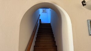 Una escalera de madera con barandilla que lleva a una habitación con pared azul y un ventanal pequeño.