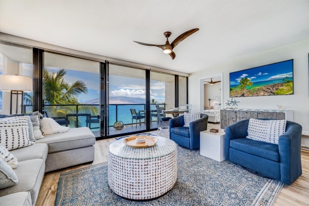 A modern living room with a sofa, armchair, coffee table, and a view of the ocean through large sliding doors.