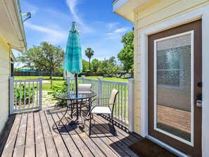 Enjoy a peaceful moment on this deck with a glass table and two chairs, surrounded by lush greenery.