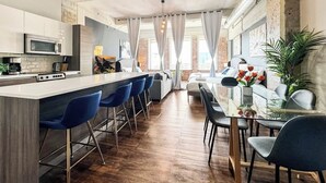 A modern kitchen with a central island, bar stools, and a dining area with a glass table and chairs.