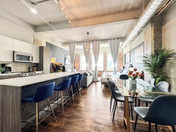 A modern kitchen with a central island, bar stools, and a dining area with a glass table and chairs.