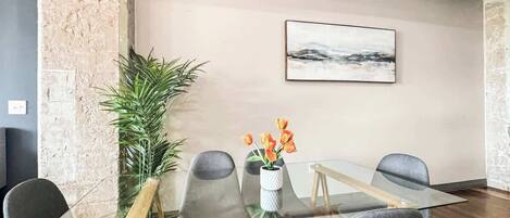 A conference room with a glass table, four grey chairs, a potted plant, and a painting on the wall.