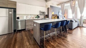 A modern kitchen with a central island, bar stools, and a dining area with a sofa.