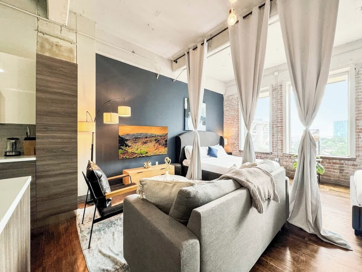 A modern bedroom with a bed, a sofa, a desk, and a large window with curtains.