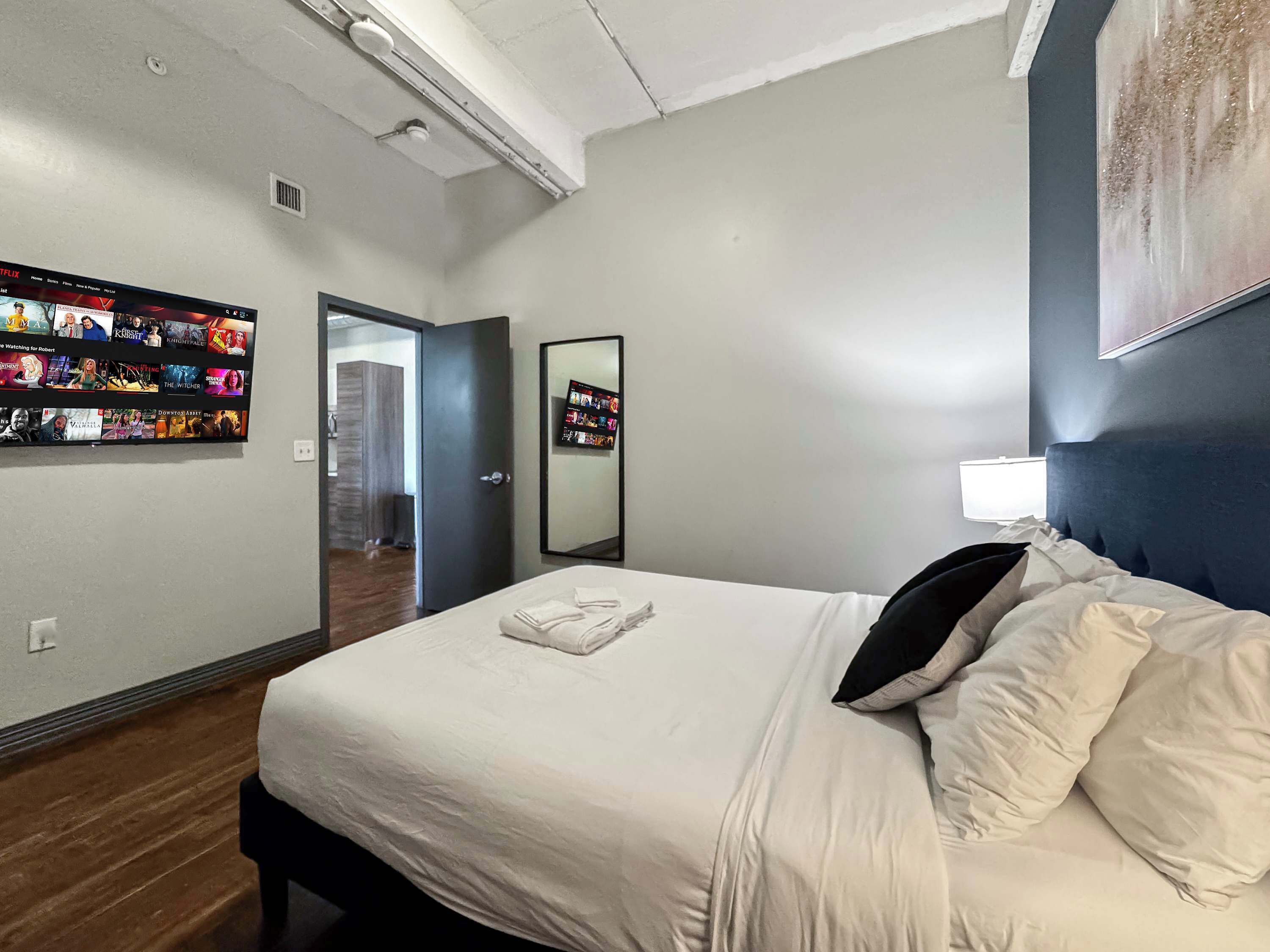 Une chambre d’hôtel avec un lit, un téléviseur fixé au mur diffusant un film, et une porte donnant accès à une salle de bain.