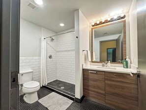Une salle de bain moderne avec des toilettes blanches, une douche dotée d’une porte en verre, un meuble-lavabo avec un miroir et un évier.