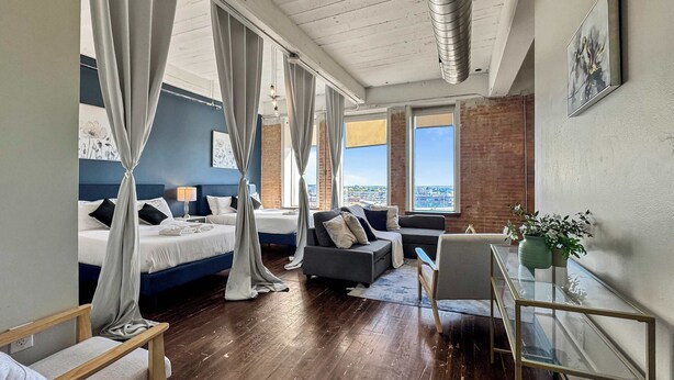 Ein modernes Hotelzimmer mit einem großen Bett, einer Couch, einem Schreibtisch und Blick auf die Stadt.