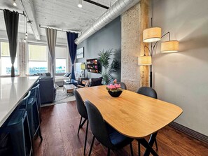 Ein modernes Wohnzimmer mit Holzesstisch, schwarzen Stühlen, einer Couch, einem Couchtisch und einem an der Wand befestigten Fernseher.