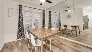 A dining area with a wooden table and white chairs, a ceiling fan, and a large mirror reflecting the room. - 2-bedroom condo in charming Dallas with WiFi, AC (Dallas)