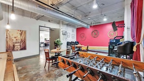 A room with a foosball table, a red wall with decorative wheels, and a jukebox. - Elegant 3BD | DT Dallas | Sleeps 16 | ValetParking (Dallas)
