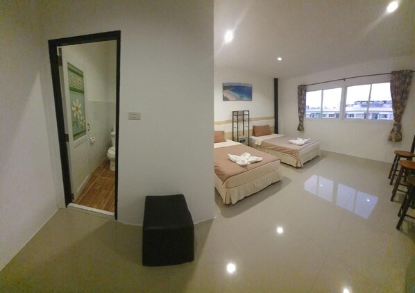 Habitación de hotel con dos camas, un espacio de descanso pequeño, ventana con vistas y puerta que da a un baño.