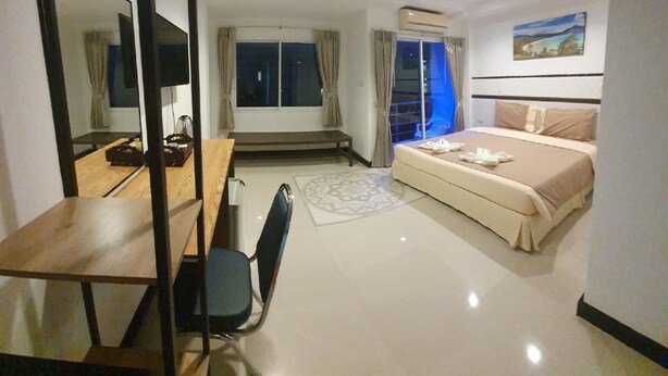 A hotel room with a bed, a desk with a chair, a TV, and a window with curtains. - Athome Hotel Nanai 8 (Patong)