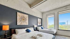 Una habitación de hotel con dos camas, un ventanal amplio y obras de arte en la pared.