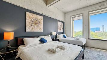 A hotel room with two beds, a large window, and artwork on the wall.