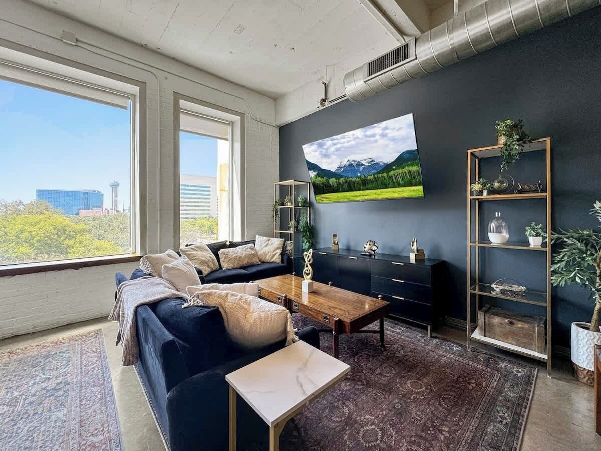 A modern living room with a dark blue sofa, a wooden coffee table, and a large flat-screen TV mounted on the wall.