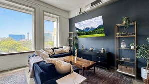 Una sala de estar moderna con un sofá azul oscuro, una mesa de centro de madera y un televisor de pantalla plana grande montado en la pared.