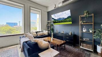 A modern living room with a dark blue sofa, a wooden coffee table, and a large flat-screen TV mounted on the wall.