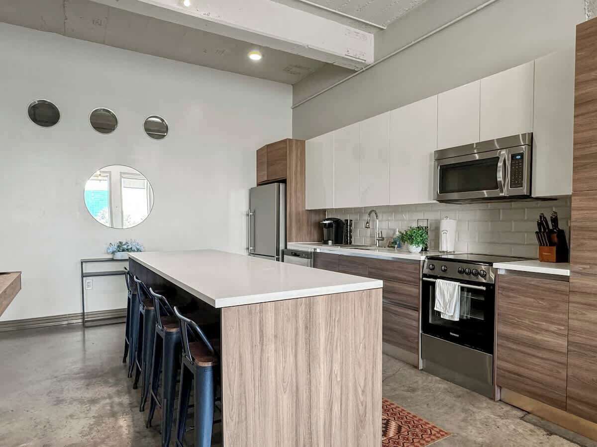 Une cuisine moderne dotée d’un îlot central, d’appareils électroménagers en acier inoxydable et d’un mur d’accent en bois.