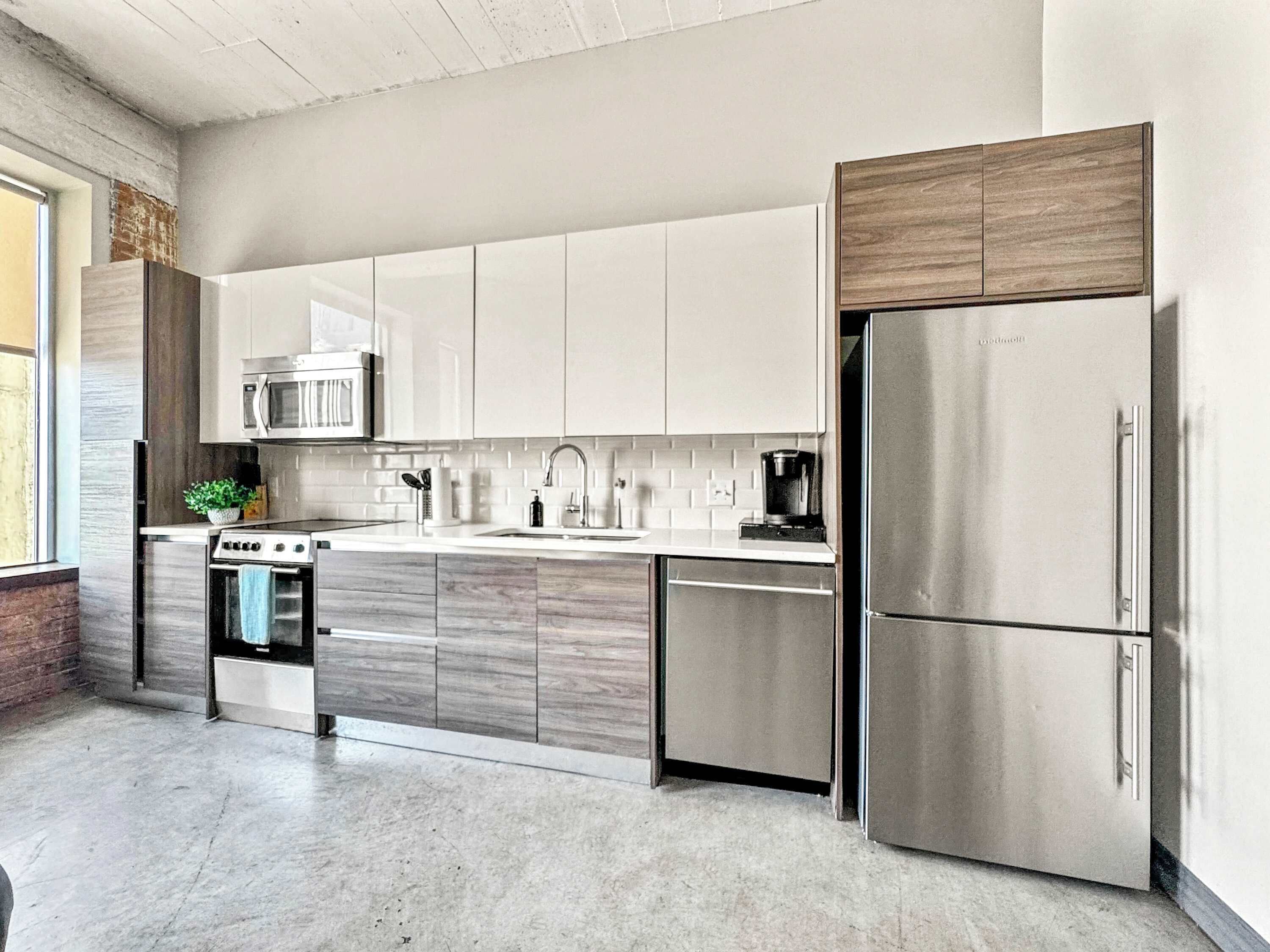 A modern kitchen with stainless steel appliances, wooden cabinets, and a large window.