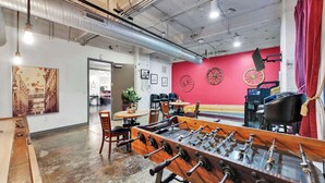A room with a foosball table, a red wall with decorative wheels, and a jukebox. - Posh 2BR Suite | Texas Core | Fits 6 | Vallet Park (Dallas)
