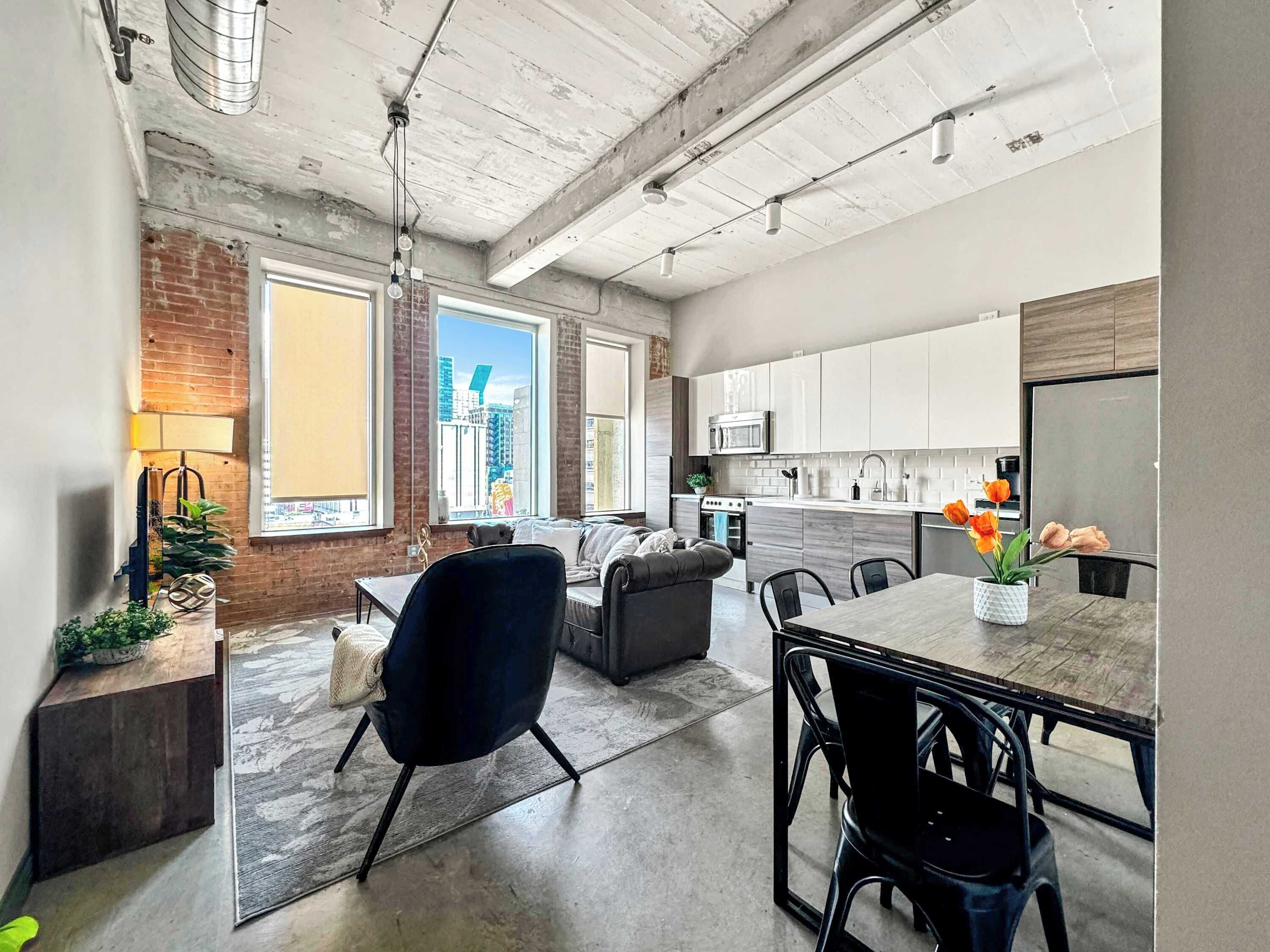A modern kitchen with white cabinets, a stainless steel refrigerator, and a dining area with a table and chairs.